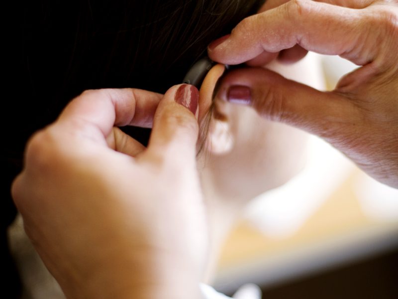 Cropped hands putting hearing aid to woman